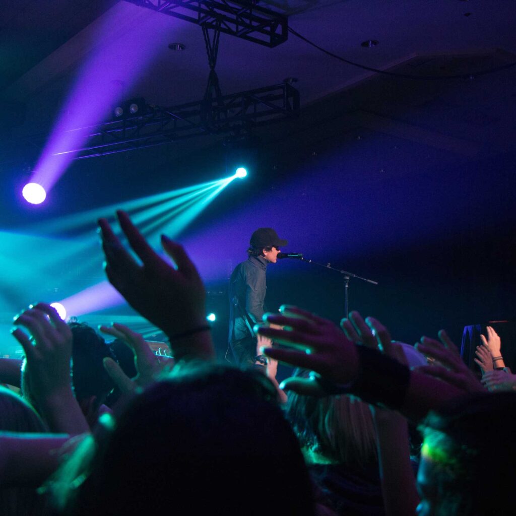 man-singing-on-stage-with-stage-lights-near-crowd-878998
